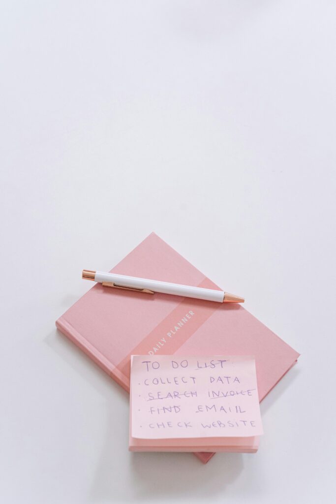 Flat lay of pink planner, pen, and sticky notes on white background.
